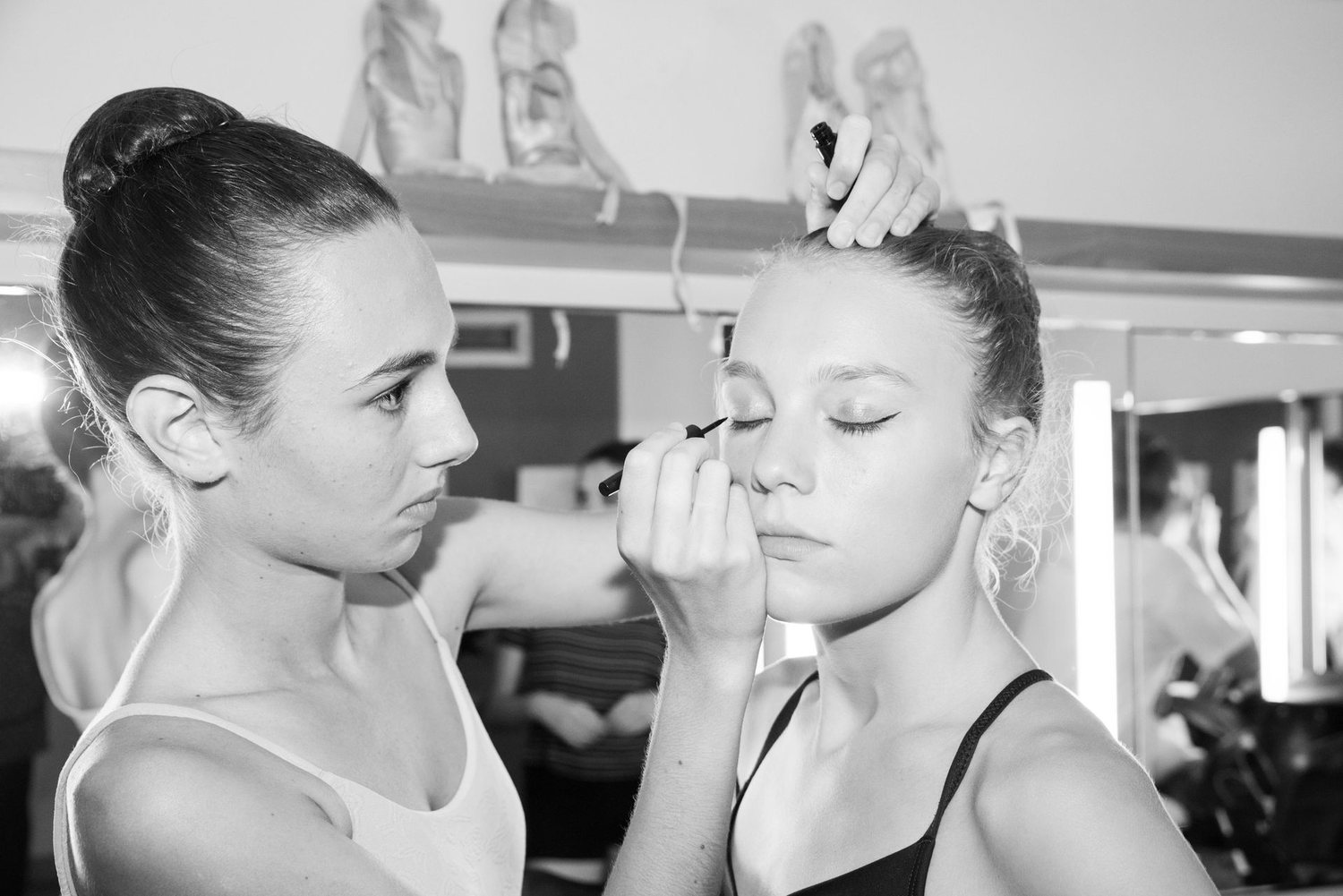 Deux danseuses en coulisses : l’une maquille l’autre devant le miroir, en noir et blanc