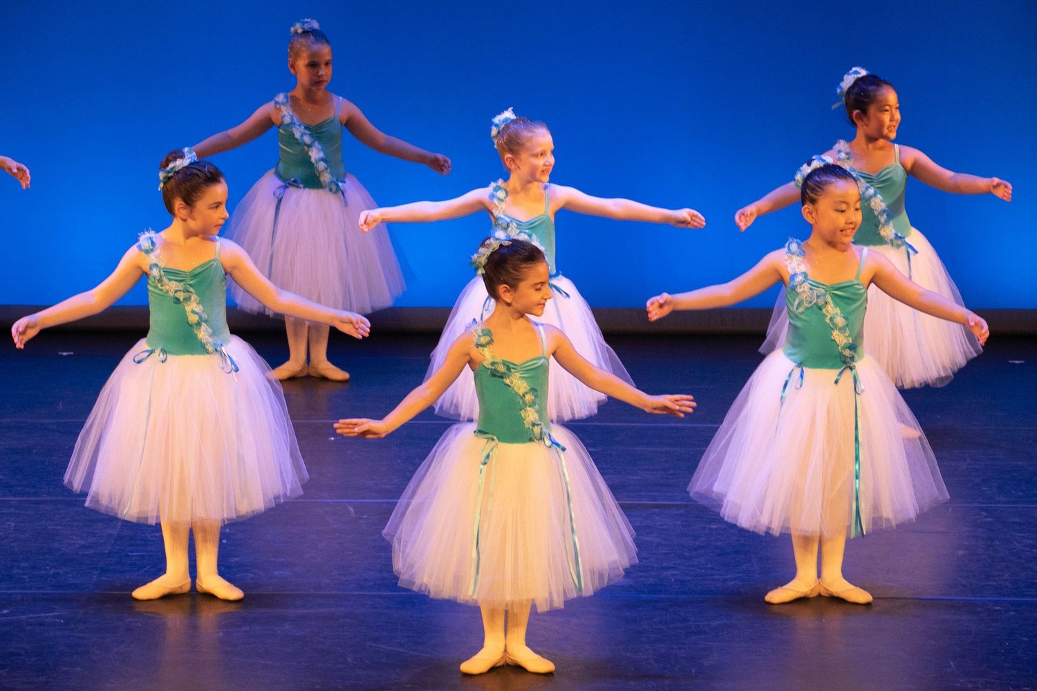 Petites danseuses en tutus rose pâle et corsages verts sur scène, devant un fond bleu