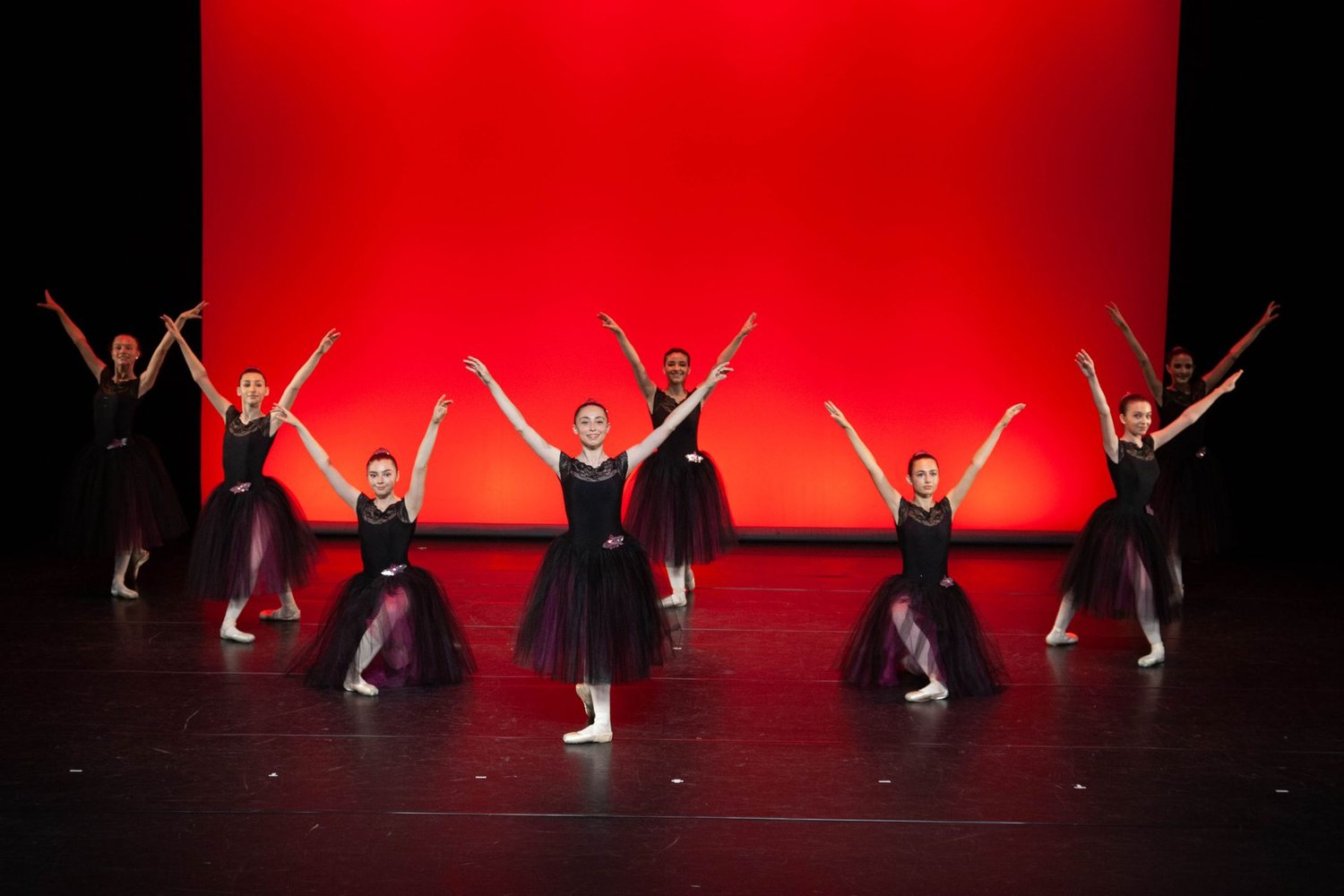 Final de spectacle : danseuses en costumes noirs devant un fond rouge